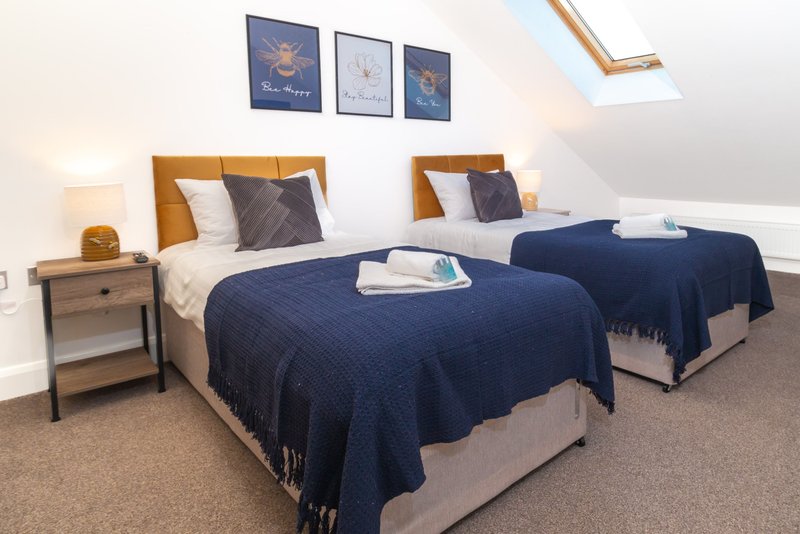 Twin bedroom with blue quilts, wooden headboards, wall art, and sloped ceiling