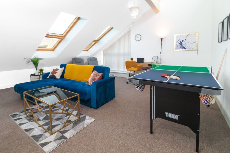 Bright attic room with blue sofa, yellow cushions, ping pong table and skylight windows