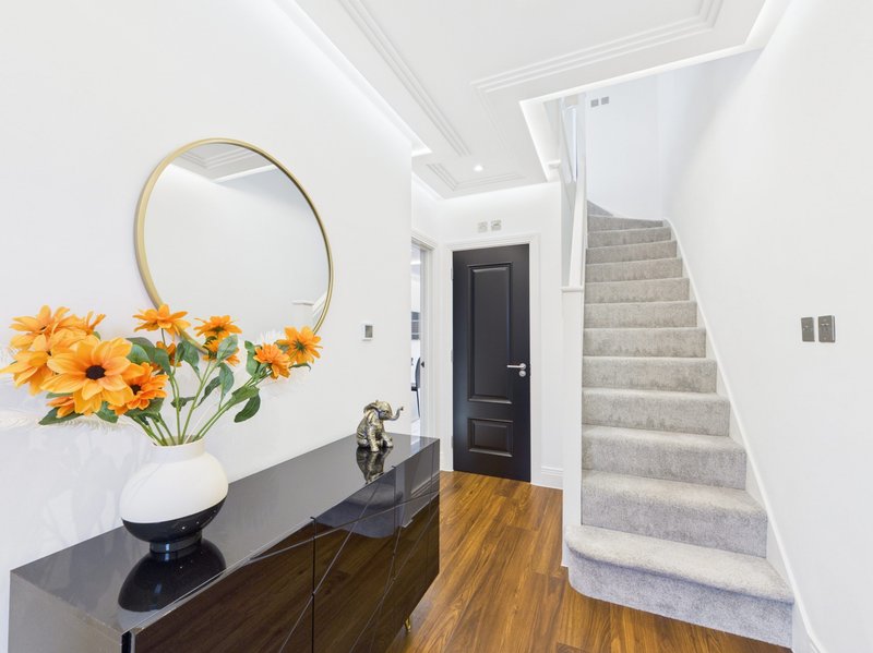 Bright hallway with round mirror, yellow flowers in vase, dark console table, and stairs