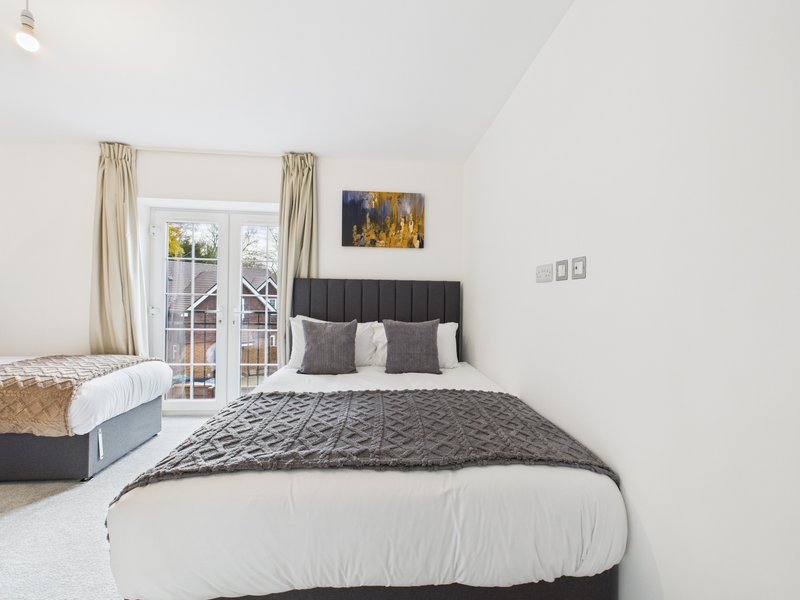 Bright bedroom with double bed, black headboard, white bedding, and French doors to garden