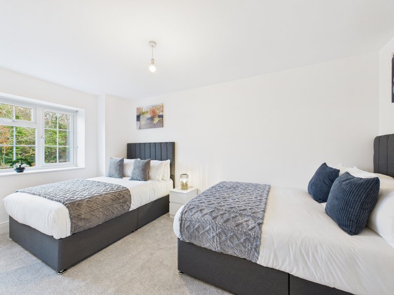 Bright bedroom with two double beds, grey upholstery, white bedding, and large windows
