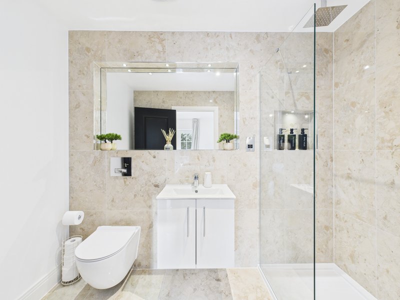 Modern bathroom with wall-mounted toilet, white vanity, large mirror, and glass shower enclosure