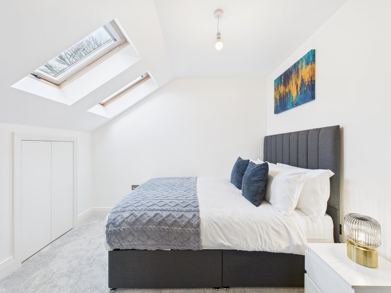 Bright bedroom with skylight, double bed, grey headboard, white pillows and blue bedding