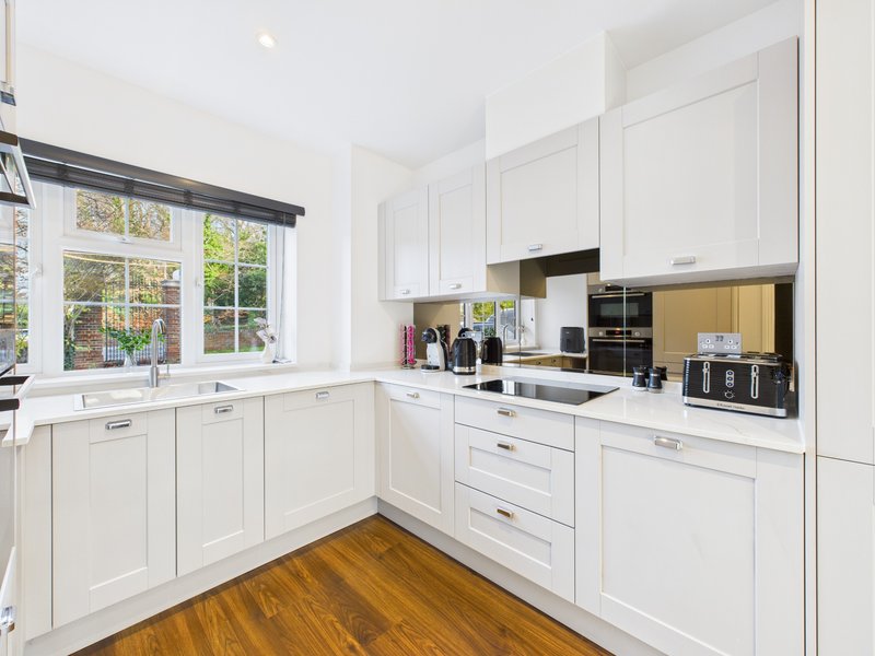 Modern white kitchen with wooden flooring, black countertops, and garden view windows