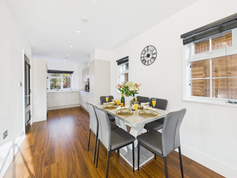 Modern open-plan kitchen and dining area with wooden flooring, white cabinetry, and dining table set for four
