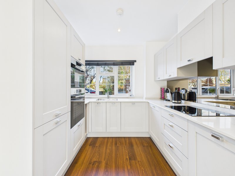 Modern white kitchen with wooden floor, stainless steel appliances and window view