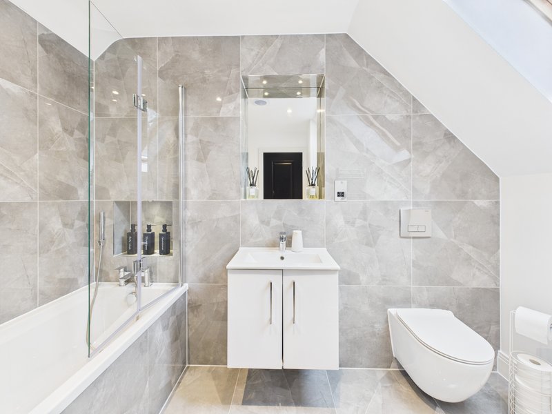 Modern bathroom with white vanity, gray tile walls, shower enclosure and toilet