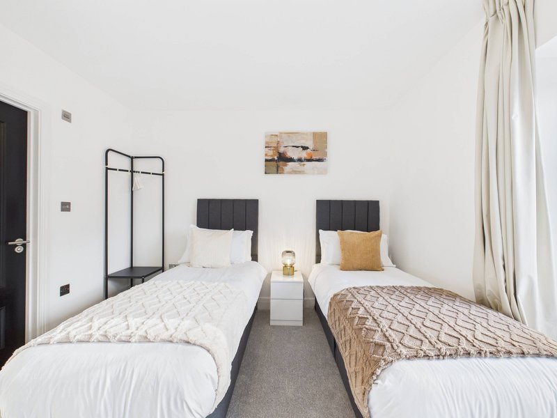Twin bedroom with two single beds, black headboards, bedside table and framed artwork on wall