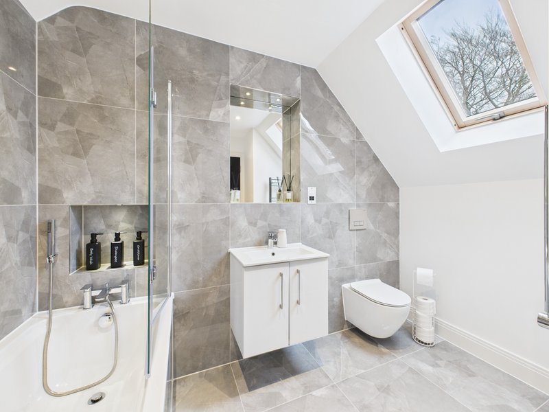 Modern ensuite bathroom with grey tile walls, white vanity, walk-in shower and skylight