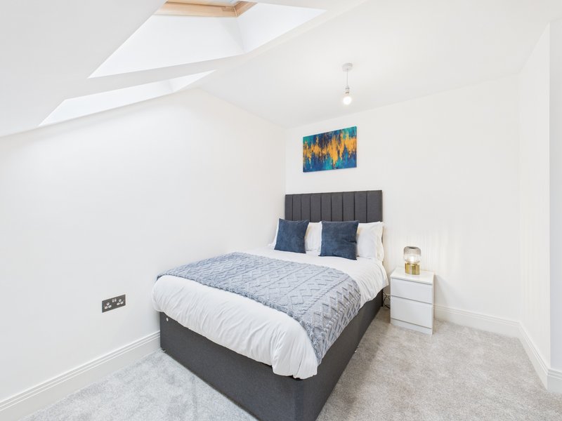 Modern bedroom with double bed, grey headboard, blue bedding, white nightstand and framed artwork