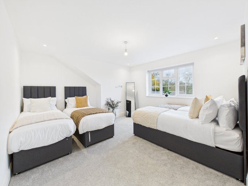 Bright bedroom with three single beds, grey headboards, white bedding, and large windows