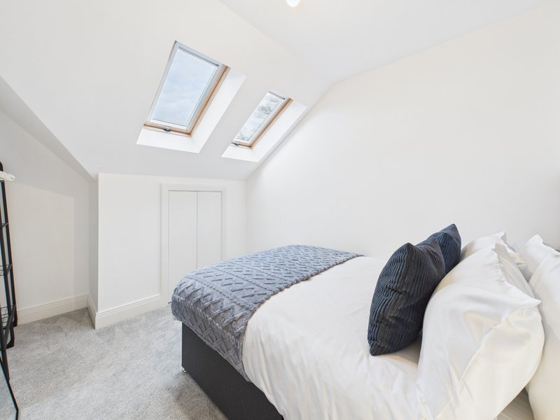 Bright bedroom with double bed, skylights, white walls and grey carpet
