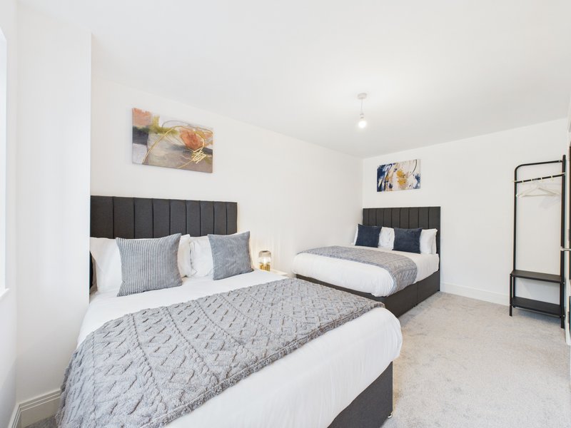 Bright bedroom with two double beds, black headboards, grey bedding and framed wall art