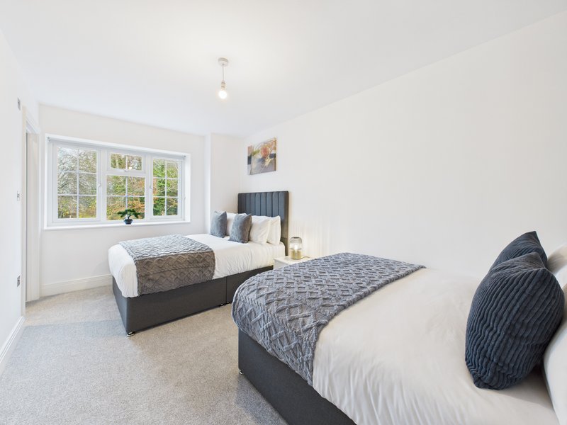Bright twin bedroom with two beds, large window, neutral décor and carpeted floor