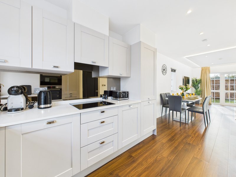 Modern white kitchen with wooden flooring, dining area visible through open plan layout