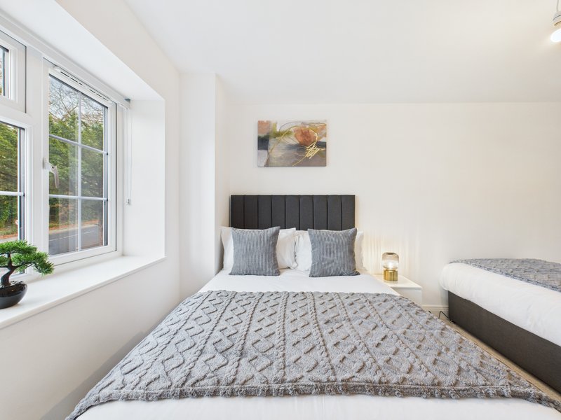 Bright bedroom with double bed, grey headboard, cushions, window with garden view