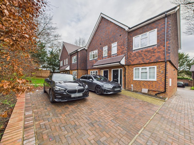 Brick semi-detached house with driveway, two parked cars, and front garden