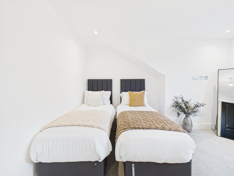 Twin bedroom with two single beds, dark headboards, and neutral bedding in bright modern room