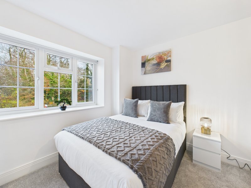 Bright bedroom with double bed, dark headboard, white bedside table and large window overlooking garden