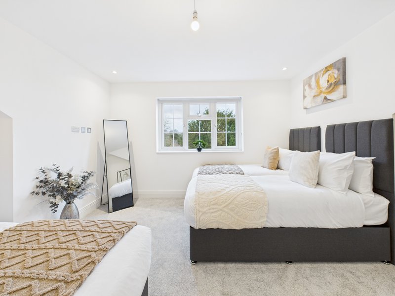 Bright bedroom with two beds, black headboards, cream bedding, mirror and window