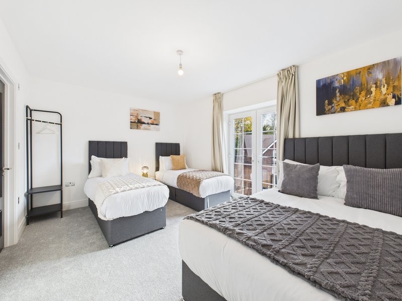 Spacious bedroom with three beds, grey headboards, white bedding, and garden doors