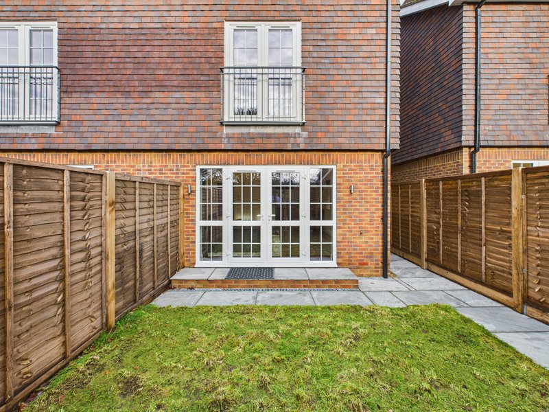 Rear garden with lawn, wooden fencing, patio area and French doors to brick townhouse