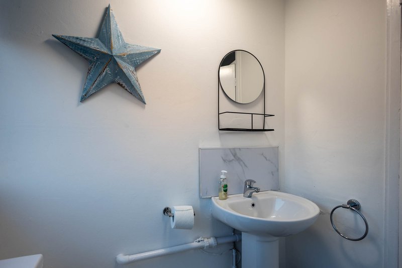 Compact bathroom with pedestal sink, round mirror, blue star decoration, and marble backsplash