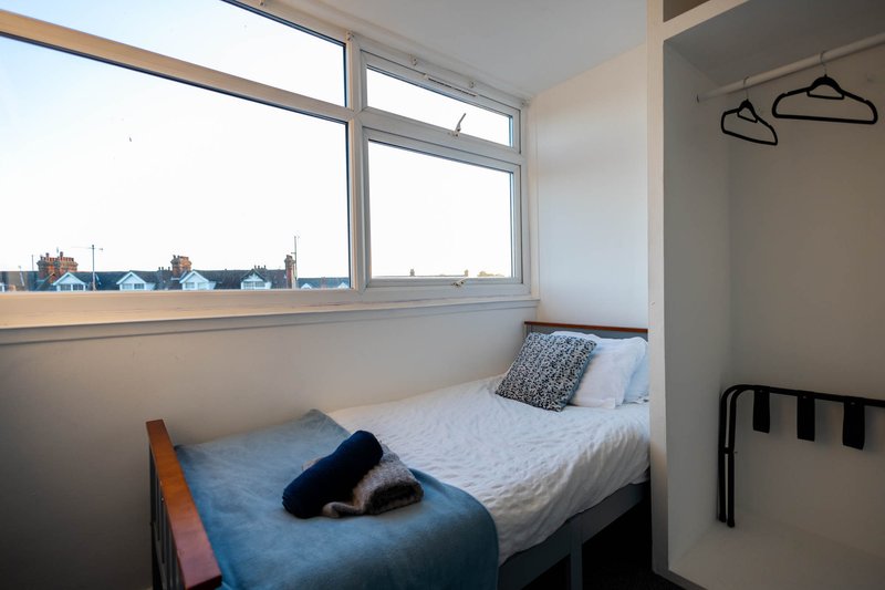 Compact bedroom with single bed, large window overlooking street, wooden hangers on wall