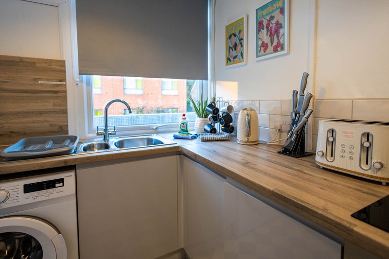 Modern kitchen with wooden worktops, white cabinetry, sink, and window overlooking street