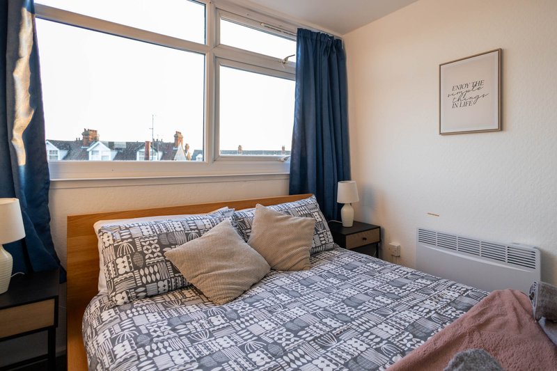Bedroom with double bed, wooden headboard, large window with city view, blue curtains