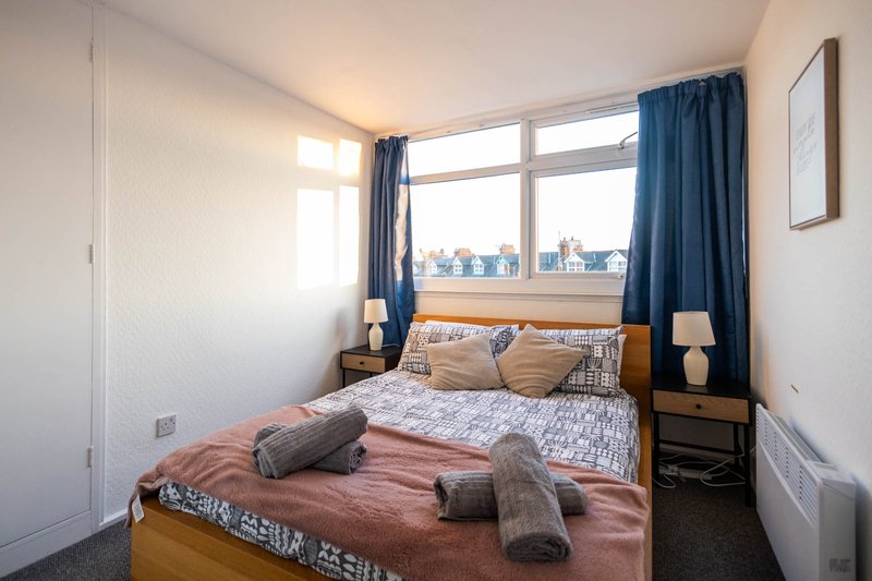 Bright bedroom with double bed, wooden frame, blue curtains and city view from window