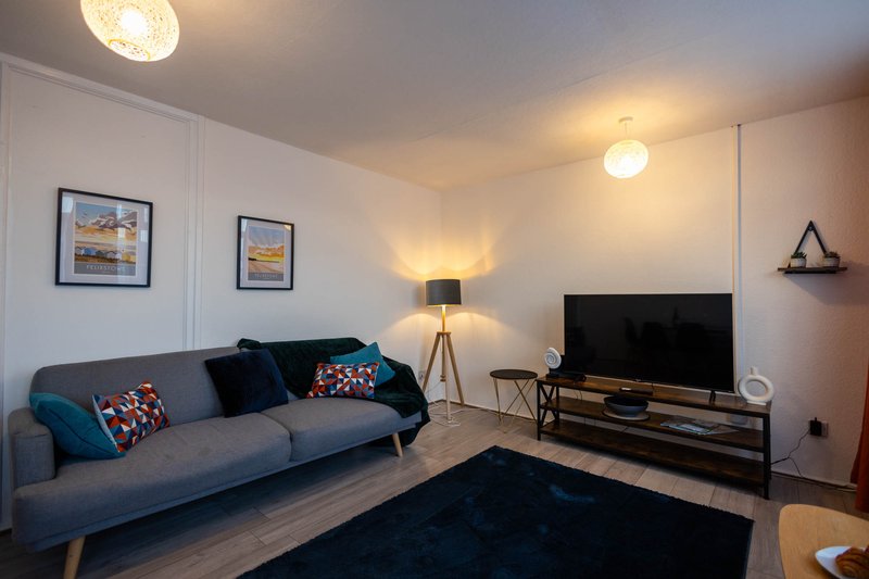 Modern living room with grey sofa, TV, tripod lamp, and framed wall art