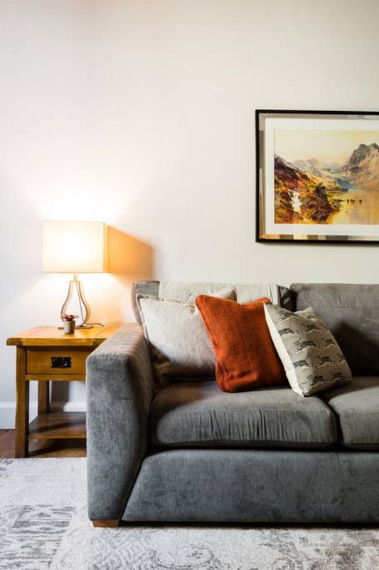 Modern living room with gray sofa, wooden side table, table lamp, and framed landscape artwork