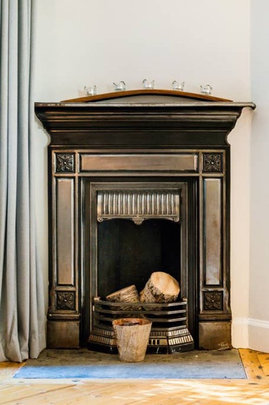 Period fireplace with ornate black surround, brass fender, and decorative items on mantelpiece