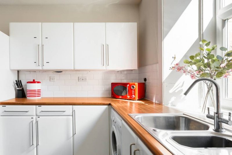 Modern kitchen with white cabinetry, wooden countertop, stainless steel sink and bright window