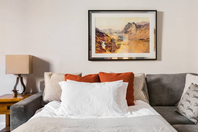 Bedroom with double bed, white pillows, orange throw, framed landscape artwork above headboard
