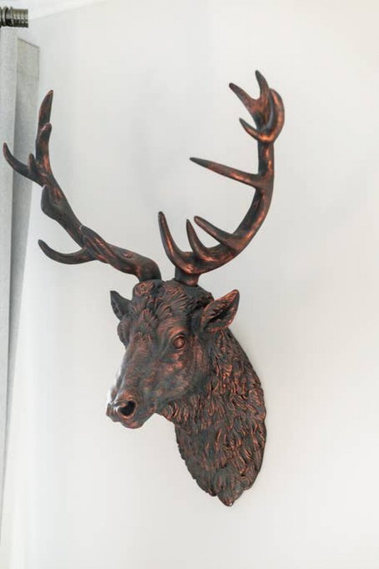 Decorative carved wooden deer head mount with antlers on white wall