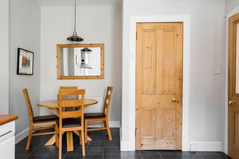 Bright kitchen with round wooden dining table, two chairs, mirror, and wooden doors