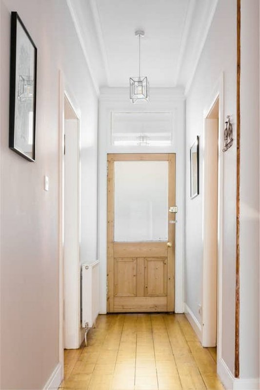 Narrow hallway with pale pink walls, wooden door, pendant light, and framed artwork