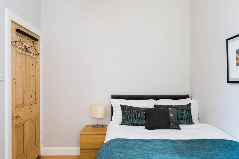 Bright bedroom with double bed, wooden door, bedside lamp and small framed picture