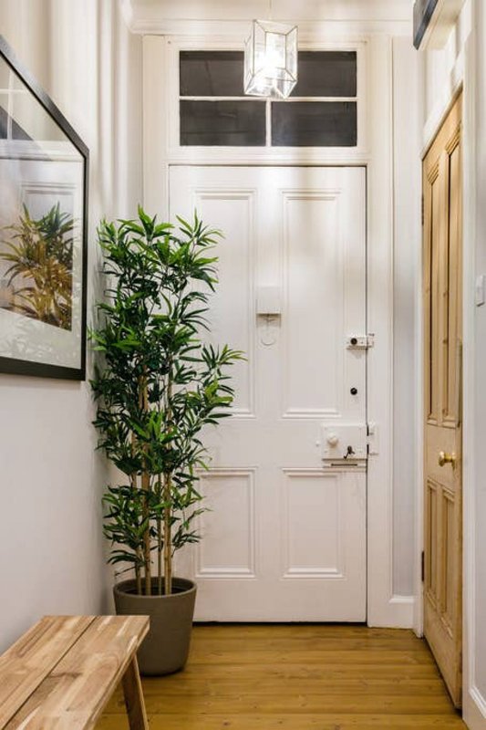 Bright hallway with white door, potted plant, wooden bench and framed wall art