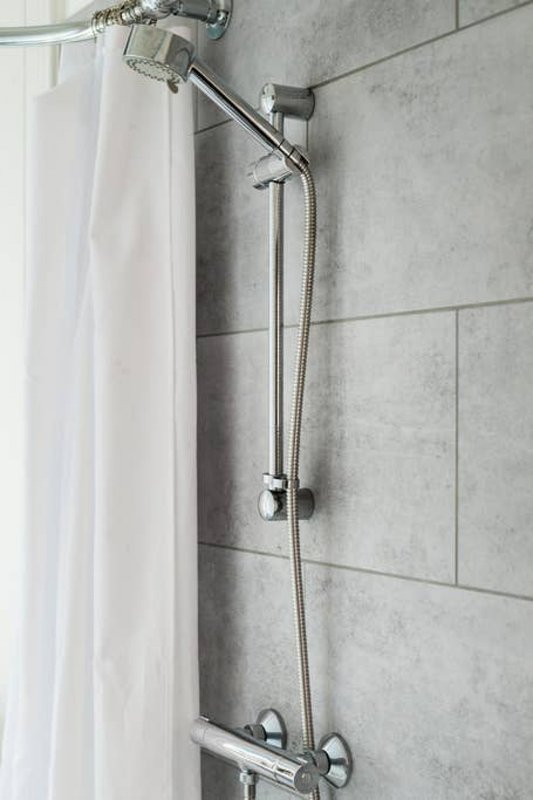 Bathroom shower wall with grey tiles, chrome fixtures, and white curtain