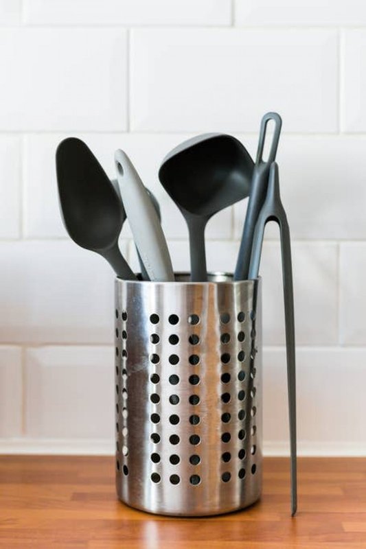 Kitchen utensil holder with cooking spoons and spatulas against white subway tile backsplash