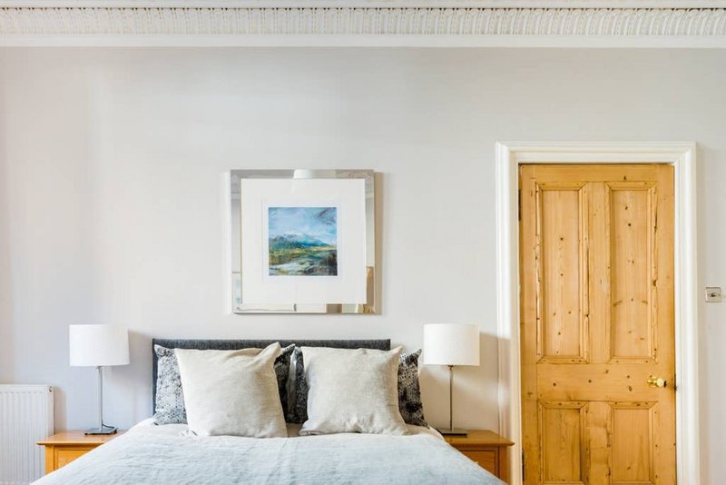 Bedroom with double bed, wooden door, framed landscape artwork, and bedside lamps