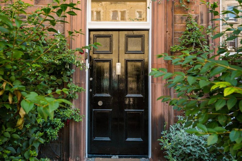 Black front door with fanlight, surrounded by climbing ivy and green foliage on brick facade