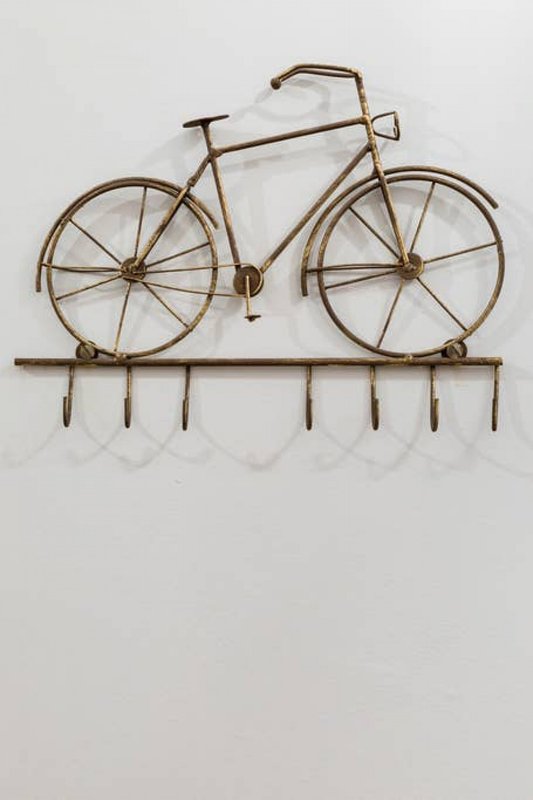 Decorative brass bicycle wall sculpture with hooks mounted on white wall