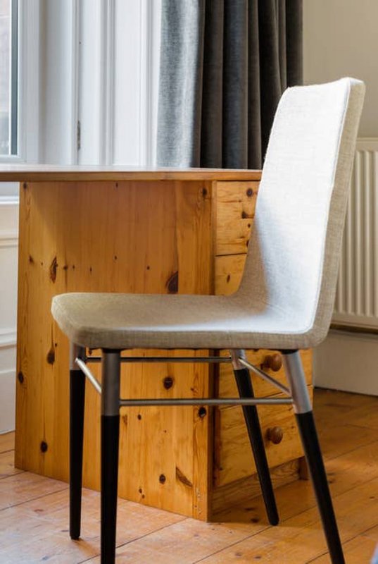 Wooden desk with white upholstered chair, curtains and radiator visible
