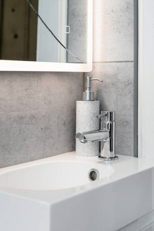 Modern bathroom sink with chrome tap, soap dispenser, and mirror above tiled backsplash