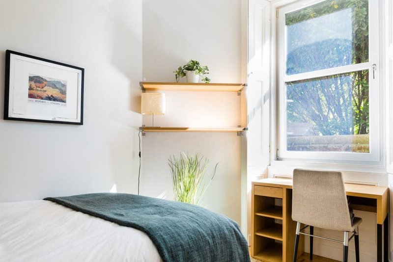 Bright bedroom with single bed, wooden desk, window with mountain view, and framed wall art