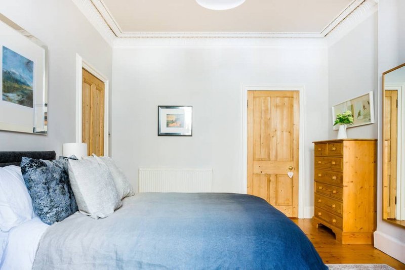 Bright bedroom with double bed, blue bedding, wooden doors and chest of drawers